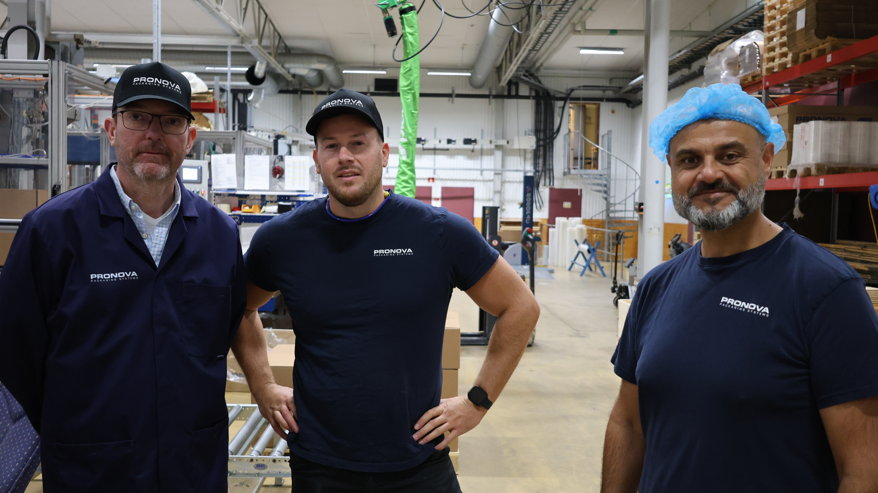 Tre m&auml;n st&aring;r i en industrilokal i bl&aring; arbetskl&auml;der och kollar in i kameran.